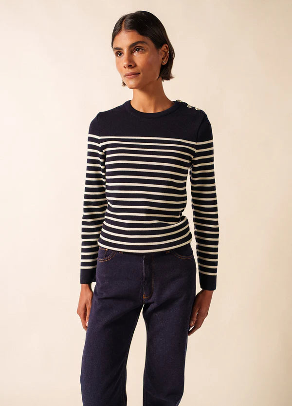 Eine Person trägt den Pullover SAINT JAMES Marée und dunkle Jeans und steht vor einem schlichten hellen Hintergrund.