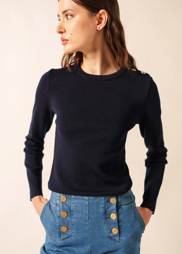 Frau in einem SAINT JAMES Marée-Pullover und hochgeschlossenen Bluejeans, Blick nach links, Hände in den Taschen.