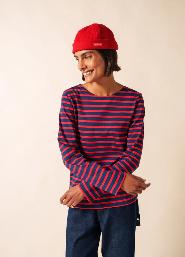Person in rotem SAINT JAMES Marin Miki und blau-rot gestreiftem Hemd lächelt mit verschränkten Armen und zeigt klassischen Seemannsstil.