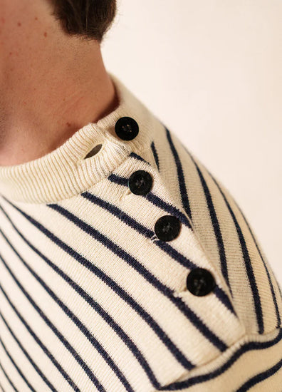 Nahaufnahme von SAINT JAMES Matelot: cremefarbener Pullover mit marineblauen Streifen und vier schwarzen Knöpfen an der Schulternaht.