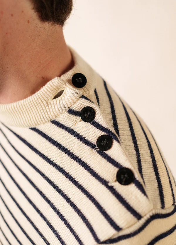 Nahaufnahme von SAINT JAMES Matelot: cremefarbener Pullover mit marineblauen Streifen und vier schwarzen Knöpfen an der Schulternaht.