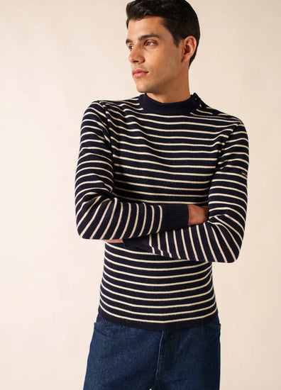 Mann in marineblau-weißem SAINT JAMES Matelot-Pullover und dunkelblauer Jeans, Arme verschränkt, Blick zur Seite.