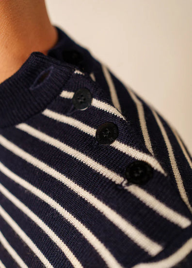 Nahaufnahme des SAINT JAMES Matelot, eines marineblauen Pullovers mit weißen Streifen und schwarzen Schulterknöpfen.