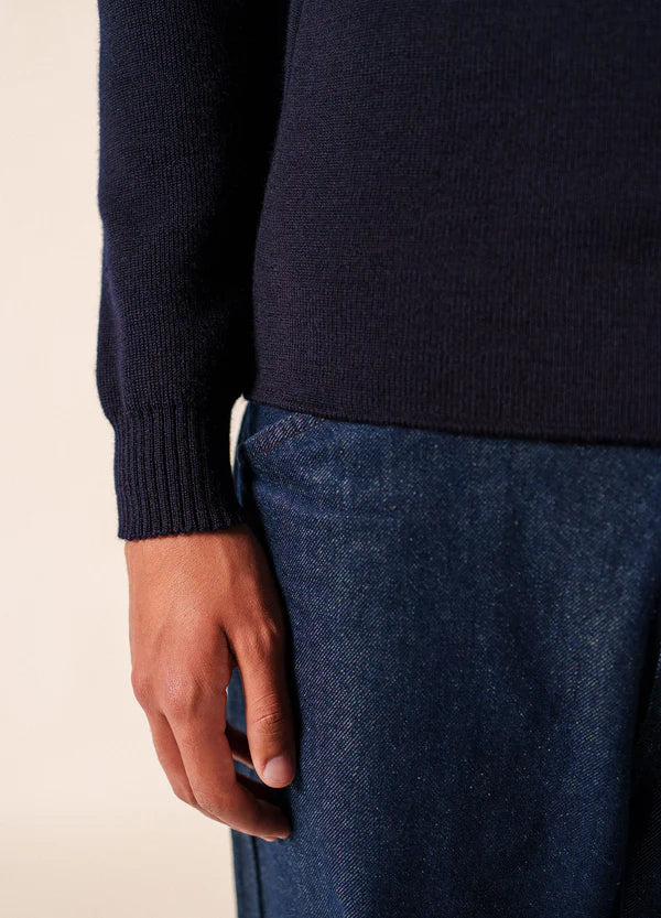 Eine Person im maritimen Modus trägt den SAINT JAMES Matelot-Pullover in Dunkelblau mit Bluejeans, den linken Arm entspannt.