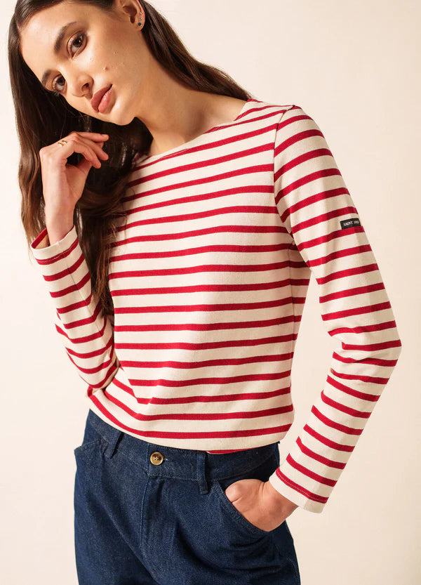 Frau im rot-weiß gestreiften Oberteil von SAINT JAMES Meridame, inspiriert vom Stil des Marinière, posiert mit der Hand vor dem Gesicht.