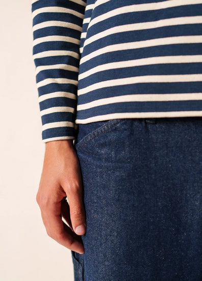 Jemand in einem marineblau-weiß gestreiften SAINT JAMES Meridien Moderne Hemd und blauen Jeans, die linke Hand an der Seite.