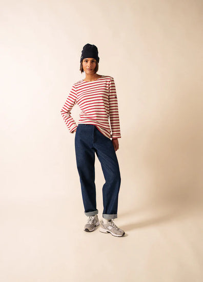 Eine Person in einem SAINT JAMES Meridien Moderne Hemd, blauen Jeans, grauen Turnschuhen und einer marineblauen Mütze steht vor einem schlichten Hintergrund.