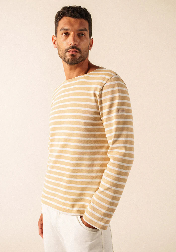 Mann, der ein beige-weiß gestreiftes langärmeliges SAINT JAMES Meridien Moderne Hemd und eine weiße Hose trägt und zur Seite schaut.