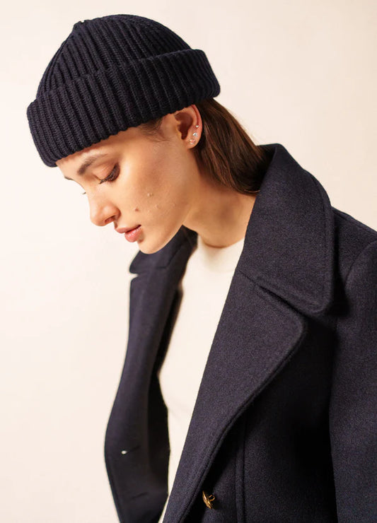 Frau in marineblauem Mantel und SAINT JAMES Miki Maille, die den bretonischen Stil vor einem neutralen Hintergrund verkörpert.