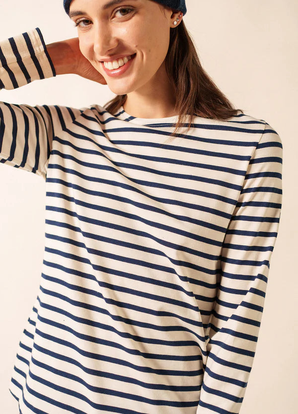 Lächelnde Frau in einem gestreiften SAINT JAMES Minquidame-Shirt und einer marineblauen Mütze, die ihren Kopf berührt.