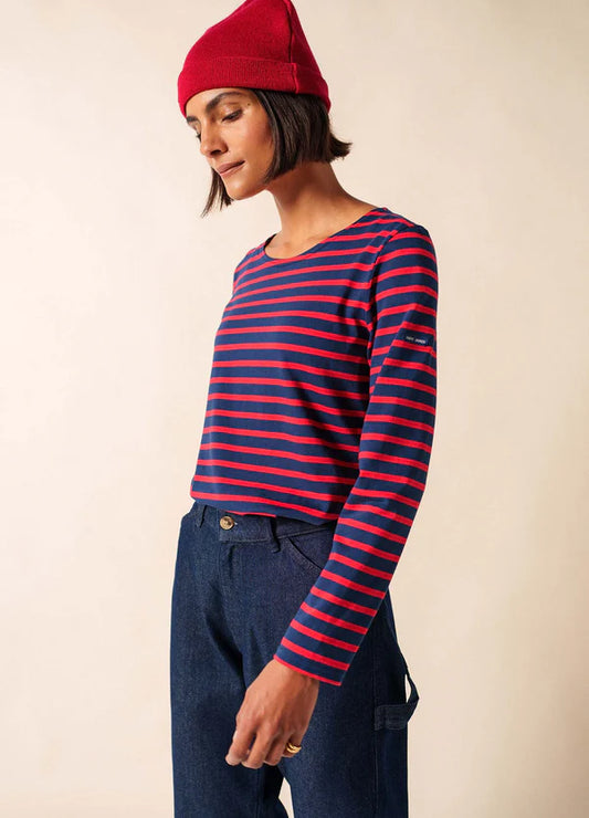 Frau mit roter Mütze und SAINT JAMES Minquidame Shirt steht vor einem hellen Hintergrund.