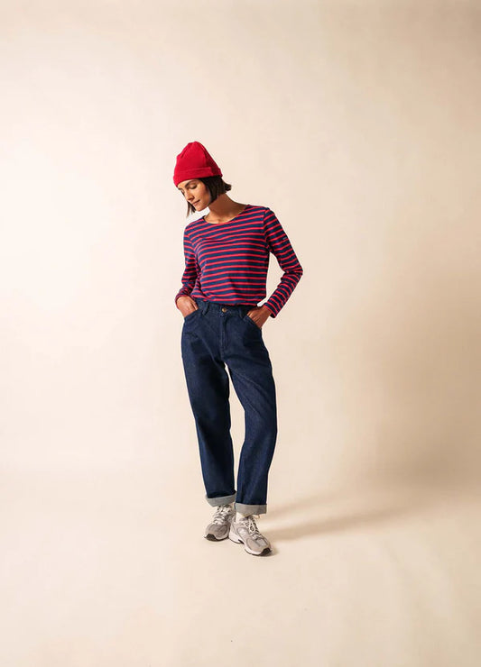 Frau mit roter Mütze, blauen Jeans und Turnschuhen, die ein SAINT JAMES Minquidame-Shirt trägt und die Hände in den Taschen hat.