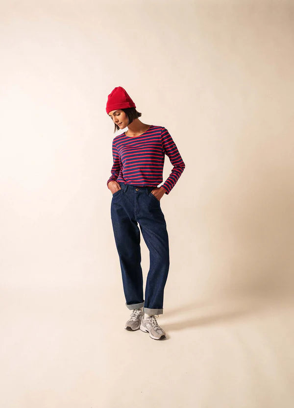 Frau mit roter Mütze, blauen Jeans und Turnschuhen, die ein SAINT JAMES Minquidame-Shirt trägt und die Hände in den Taschen hat.