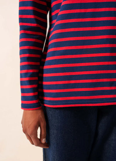 Eine Person trägt ein marineblau-rot gestreiftes, langärmeliges SAINT JAMES Minquidame-Hemd und dunkelblaue Jeans, eine Hand ist sichtbar.