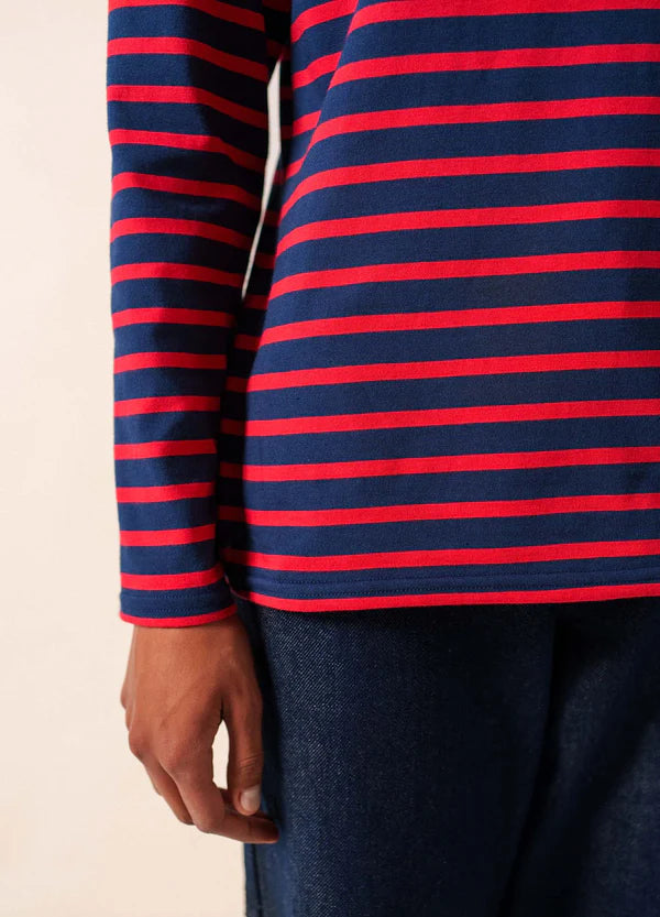 Eine Person trägt ein marineblau-rot gestreiftes, langärmeliges SAINT JAMES Minquidame-Hemd und dunkelblaue Jeans, eine Hand ist sichtbar.