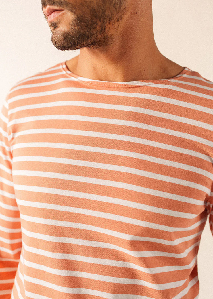 Mann trägt SAINT JAMES Minquiers, orange-weiß gestreiftes Baumwoll-Langarmhemd, gezeigt von der Schulter bis zur oberen Brust.