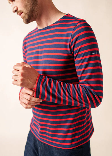Mann trägt SAINT JAMES Minquiers marineblau-rot gestreiftes langärmeliges Hemd mit dunkler Hose vor einem hellen Hintergrund.