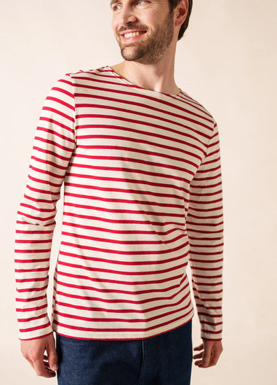 Lächelnder Mann in einem weißen, langärmeligen SAINT JAMES Minquiers-Hemd mit roten Streifen und blauen Jeans.