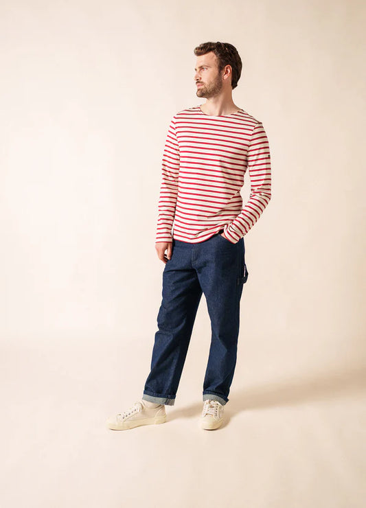 Mann in SAINT JAMES Minquiers-Hemd, blauen Jeans und weißen Turnschuhen steht vor einem beigen Hintergrund.