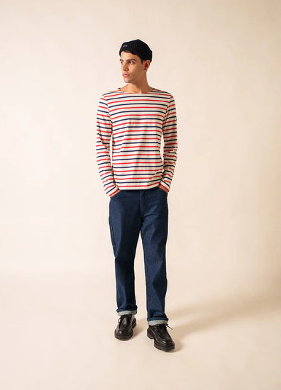 Ein Mann in einem gestreiften SAINT JAMES Minquier Tri Hemd, einer dunklen Jeans und einer Mütze trägt einen französischen Unisex-Look.