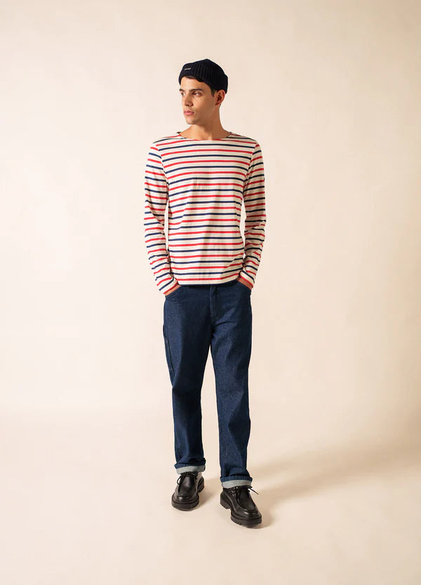 Ein Mann in einem gestreiften SAINT JAMES Minquier Tri Hemd, einer dunklen Jeans und einer Mütze trägt einen französischen Unisex-Look.