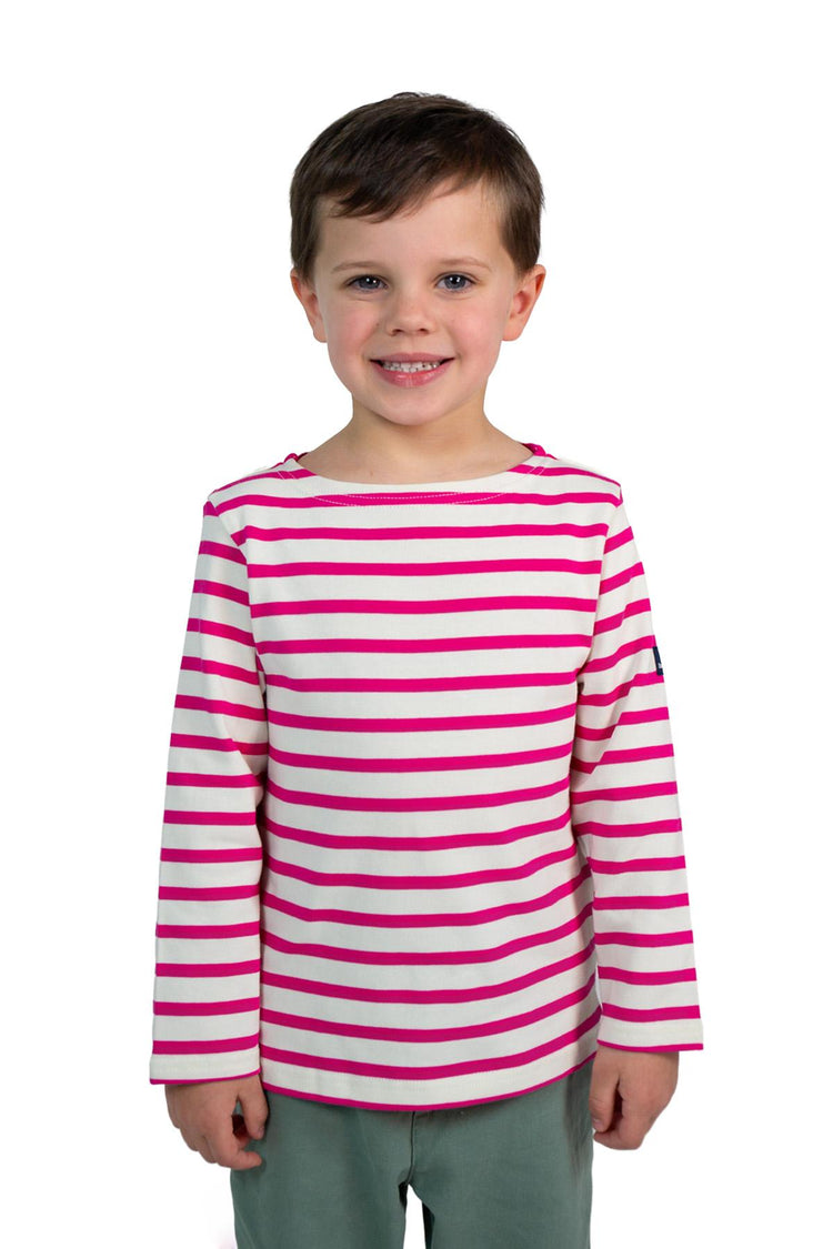 Lächelndes Kind in MOUSQUETONs Mario Kid, rosa gestreiftes Oberteil und grüne Hose, steht vor einem weißen Hintergrund.