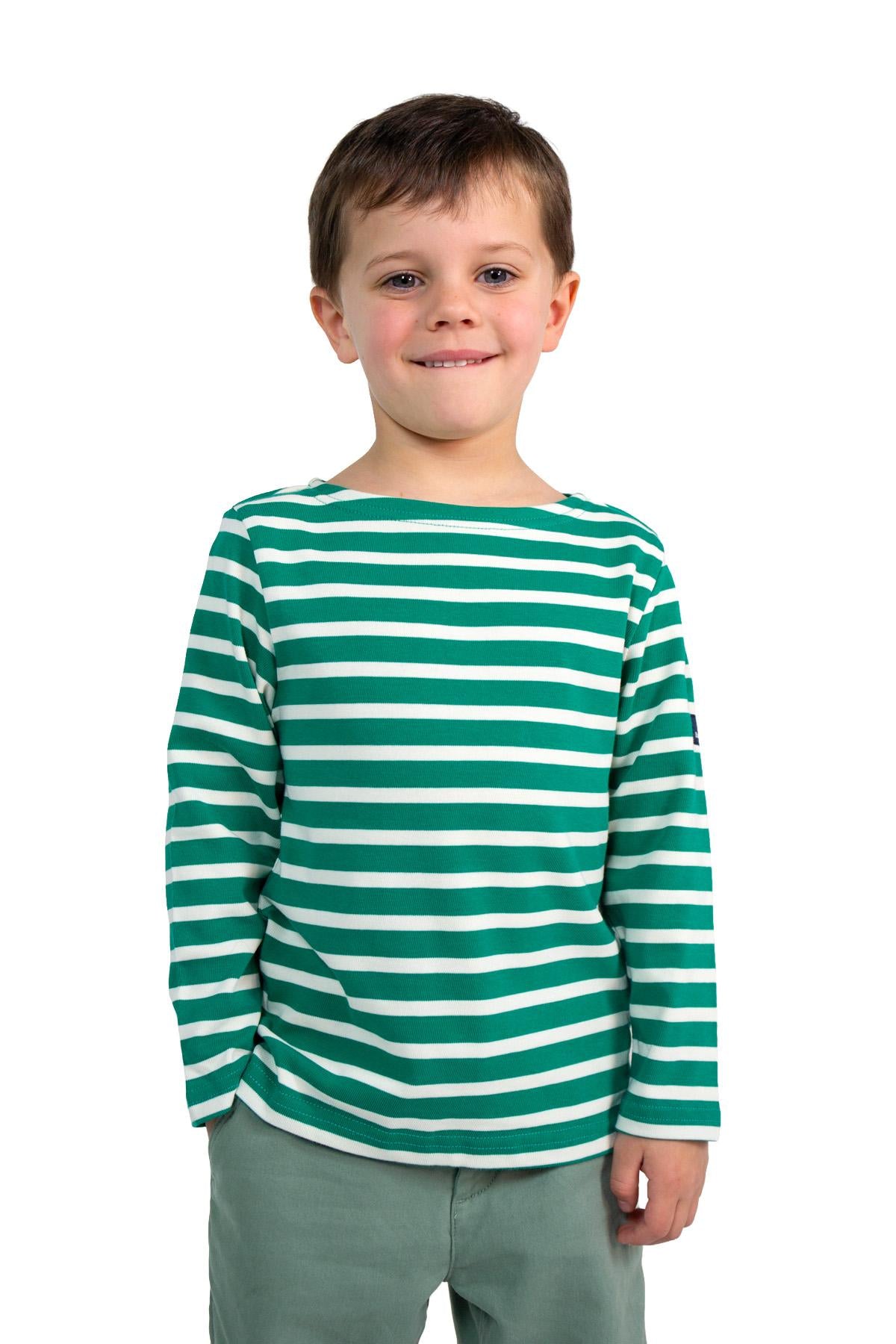 Lächelnder Junge in einem MOUSQUETON Mario Kid grüner Baumwollmarinière, stehend vor einem weißen Hintergrund.