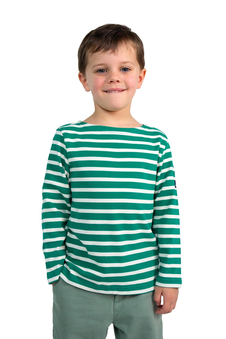 Lächelnder Junge in einem MOUSQUETON Mario Kid grüner Baumwollmarinière, stehend vor einem weißen Hintergrund.