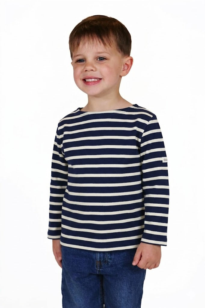 Lächelnder Junge in einem MOUSQUETON Mario Kid Marinière und blauen Jeans, stehend vor einem weißen Hintergrund.