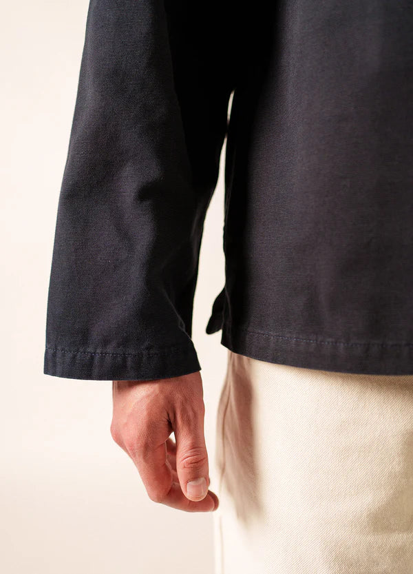 Nahaufnahme der linken Hand einer Person, die die Jacke SAINT JAMES Nemo und eine leichte Hose aus Segeltuchstoff trägt, die die maritime Tradition vor einem neutralen Hintergrund widerspiegelt.