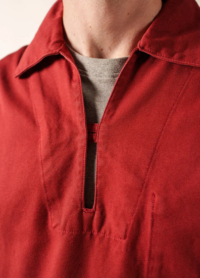 Nahaufnahme einer Person, die das rote Hemd mit Kragen Nemo von SAINT JAMES über einem grauen T-Shirt trägt. Es ist von der maritimen Tradition inspiriert und hat einen V-Ausschnitt mit sichtbaren Nähten am unteren Hals und auf der oberen Brust.