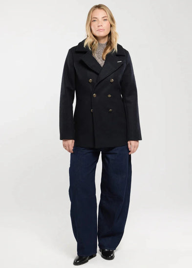 Eine Frau trägt den Mantel Pointe du Raz von ARMOR LUX, einen schwarzen Wollmantel mit Reverskragen, über einem grauen Pullover und Jeans.
