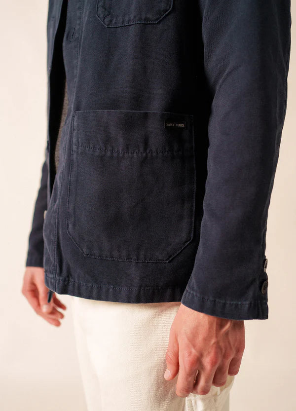 Eine Person in einer marineblauen SAINT JAMES-Sirocco-Jacke mit einer großen Vordertasche und einer weißen Hose, mit dem Oberkörper nach unten dargestellt.