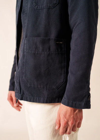 Eine Person in einer marineblauen SAINT JAMES-Sirocco-Jacke mit einer großen Vordertasche und einer weißen Hose, mit dem Oberkörper nach unten dargestellt.