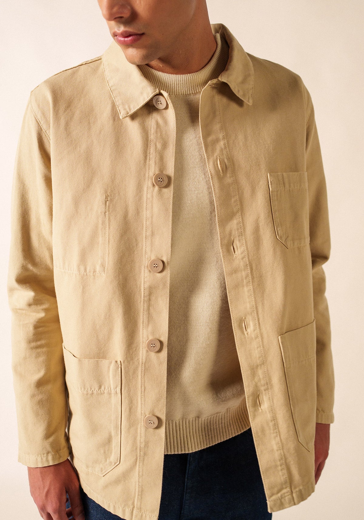 Mann, der die beige SAINT JAMES Sirocco-Jacke über einem cremefarbenen Pullover und einer dunklen Hose trägt und zur Seite schaut.