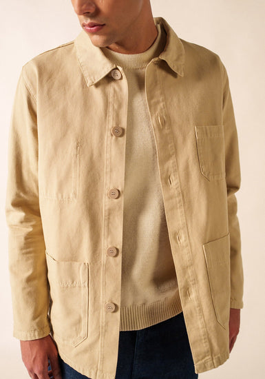 Mann, der die beige SAINT JAMES Sirocco-Jacke über einem cremefarbenen Pullover und einer dunklen Hose trägt und zur Seite schaut.