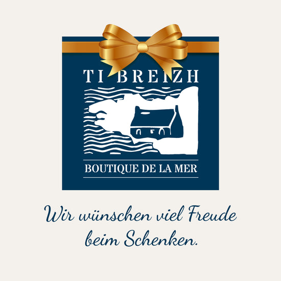 Boutique de la Mer Gutschein: blaue Karte mit goldener Schleife, Küstenszene und deutschem Text "Wir wünschen viel Freude beim Schenken.