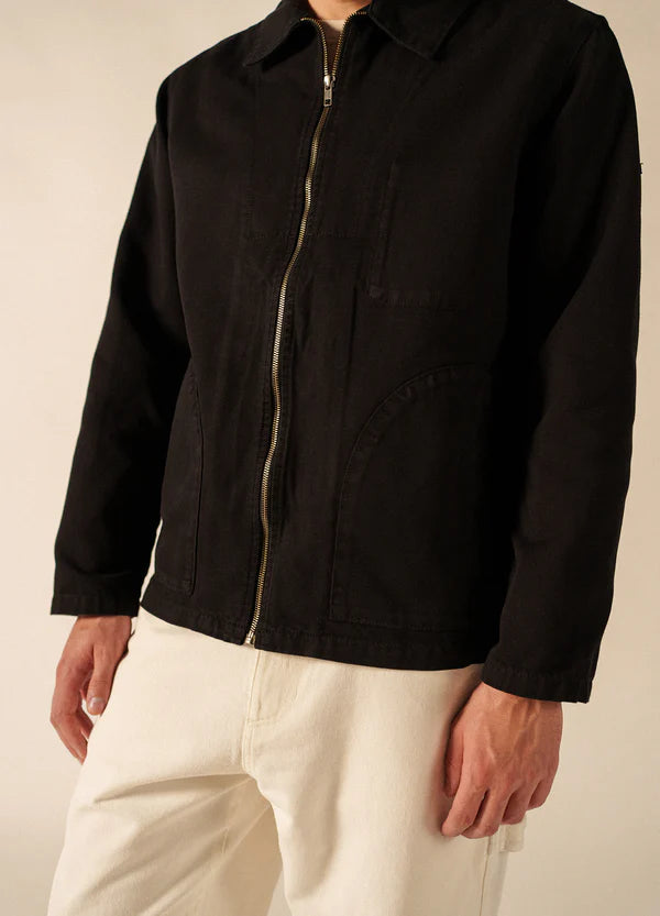 Eine Person in einer schwarzen SAINT JAMES Zephyr-Jacke und einer cremefarbenen Hose, die von den Schultern bis zur Mitte der Oberschenkel reicht.
