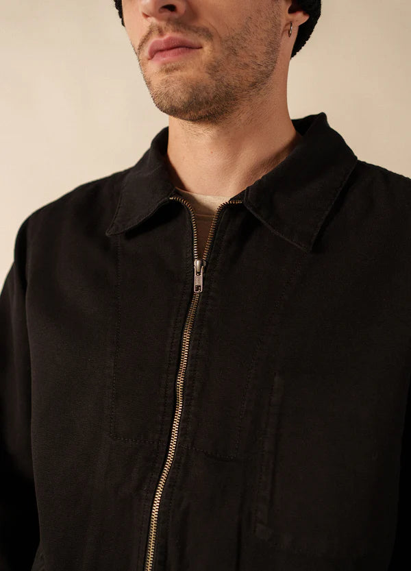 Mann, der eine schwarze SAINT JAMES Zephyr Jacke mit Reißverschluss und eine schwarze Mütze trägt, von den Schultern aufwärts gezeigt.