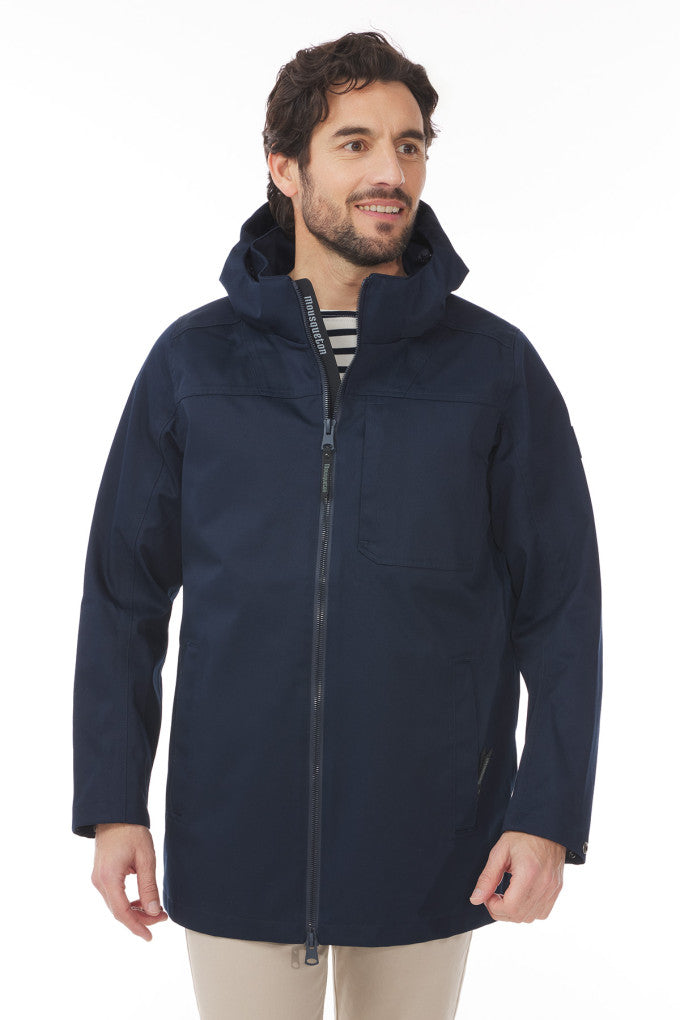 Mann in marineblauem Mousqueton Ardan-Parka mit Isolierung, gestreiftem Hemd und heller Hose, stehend und lächelnd.