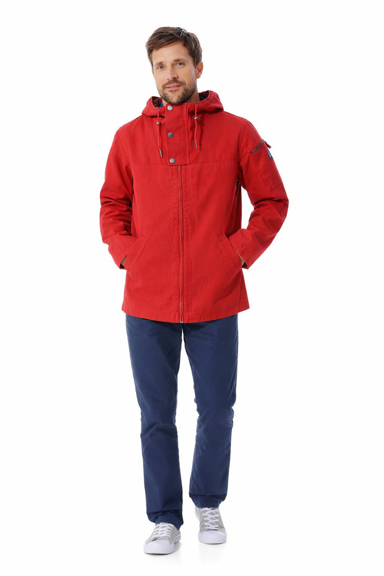 Mann in roter MOUSQUETON Kapuzenjacke "Baden", blauer Hose und grauen Sneakers vor weißem Hintergrund.