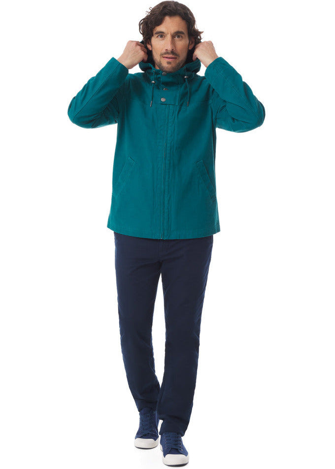 Ein Mann, der eine blaugrüne MOUSQUETON-Baden-Jacke, eine marineblaue Hose und Turnschuhe trägt, steht und richtet seine Kapuze.