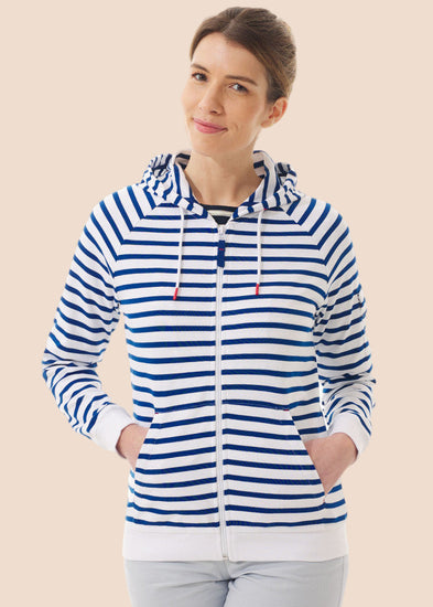 Frau lächelt in dem gestreiften Baumwoll-Kapuzenpullover Mulane von MOUSQUETON mit Kängurutaschen vor einem beigen Hintergrund.