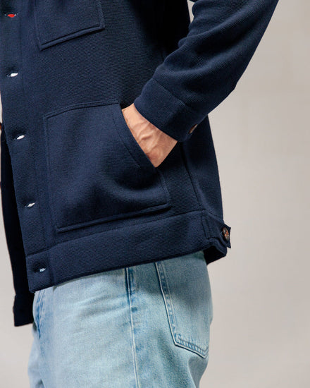 Person, die eine marineblaue Jacke von ROYAL MER Lois und hellblaue Jeans trägt, eine Hand in der Tasche, von der Seite gezeigt.
