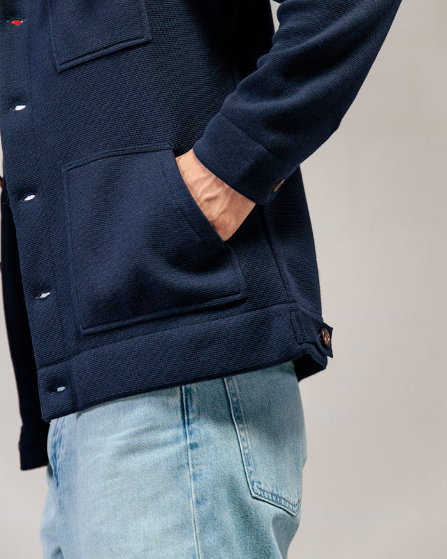 Person, die eine marineblaue Jacke von ROYAL MER Lois und hellblaue Jeans trägt, eine Hand in der Tasche, von der Seite gezeigt.
