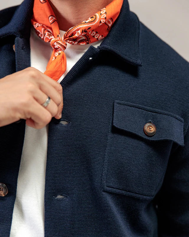 Model in der „Lois“-Jacke von ROYAL MER, weißem Hemd und orangefarbenem Bandana, mit silbernem Ring, das den Kragen zurechtzieht.
