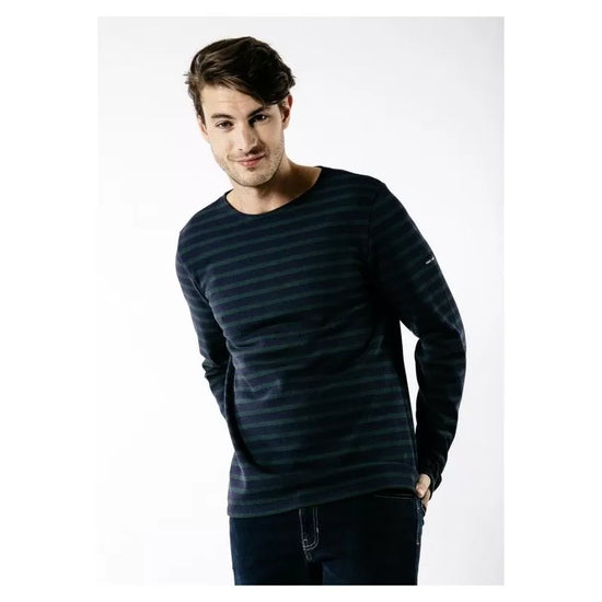 Ein Mann in einem gestreiften langärmeligen SAINT JAMES Meridien Moderne Hemd und Jeans steht lächelnd vor einem weißen Hintergrund.